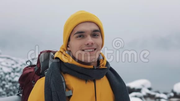 穿着冬装的年轻迷人男子的肖像穿着黄色冬装的徒步旅行者看着摄像机视频的预览图