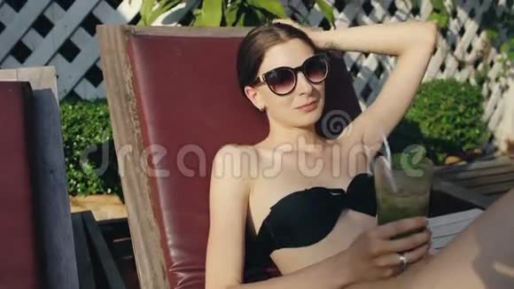 幸福的女人坐在酒店的游泳池旁喝着异国情调的鸡尾酒视频的预览图