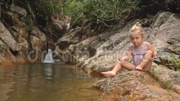 小金发姑娘在瀑布边的石头上寻找水果视频的预览图