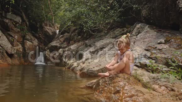 小金发女孩清洁脚手指站在瀑布旁视频的预览图