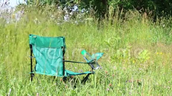 一张野餐椅矗立在一片轻浮的草地上草本植物和花朵从夏风中摇摆视频的预览图