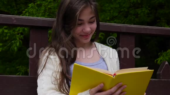 欢快的少女读书的肖像春天坐在森林的长凳上在户外学习高清视频视频的预览图