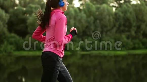 一个穿着粉色夹克的女孩正在准备跑步热身通过电话用耳机听音乐视频的预览图