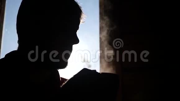 年轻人在窗户附近放松在阳光下喝着蒸汽热茶动作缓慢视频的预览图