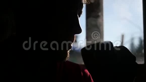 一个蓄着胡须的成年人坐在窗前喝着一杯热气腾腾的热茶慢慢地视频的预览图