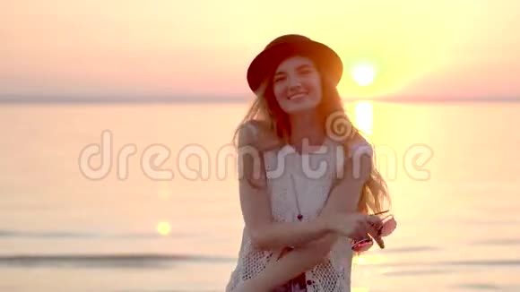 戴着帽子的漂亮金发女人在海上享受暑假金色的日落视频的预览图