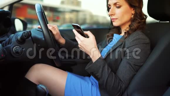 一个穿着蓝色连衣裙和夹克的女人在车里用智能手机视频的预览图