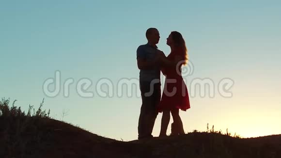 一对幸福的年轻夫妇的剪影和日落时在外面慢舞的狗慢动作视频男人和女孩视频的预览图