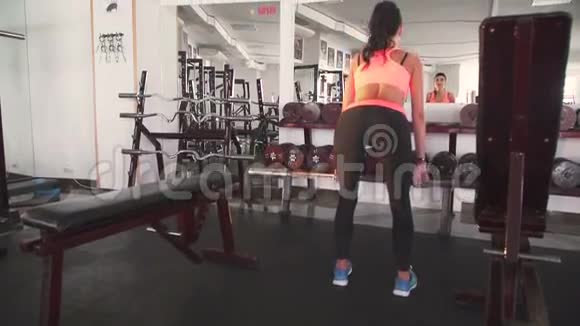 在健身房里用杠铃蹲下的女孩回头看慢慢地视频的预览图