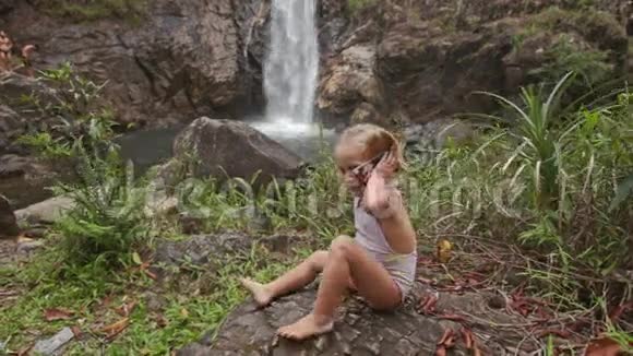 特写小女孩在瀑布上通过电话发言视频的预览图