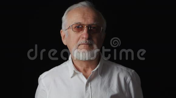 在黑色背景下穿着白色衬衫的老人的特写肖像视频的预览图