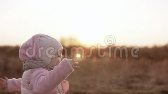 小女孩穿着粉红色的衣服慢动作地奔跑着笑着看日落视频的预览图