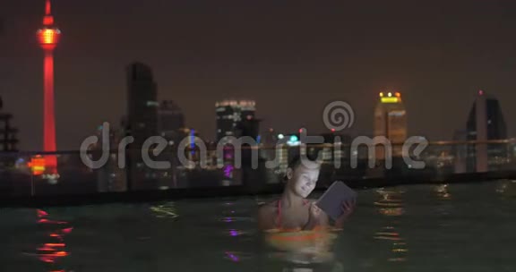 在吉隆坡一家酒店的屋顶上马来西亚正在游泳的年轻女孩和在平板电脑上工作视频的预览图