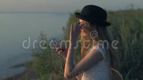 年轻女孩用智能手机坐在河边的悬崖边上视频的预览图