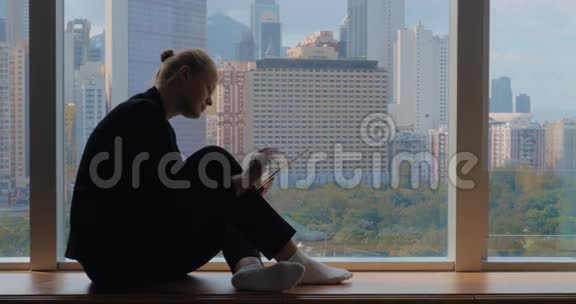 年轻的女人坐在窗台上用平板电脑看着窗户中国香港视频的预览图