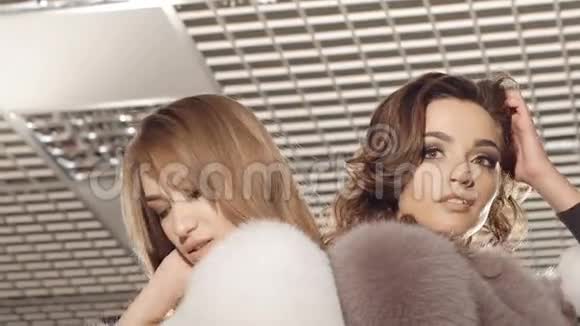 两个穿着毛皮外套的女孩在时尚丰富的精品店里摆姿势慢慢地视频的预览图