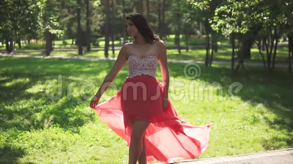 夏天公园里穿着红色连衣裙和高跟鞋的漂亮女孩裙子在风中飘扬慢动作视频的预览图