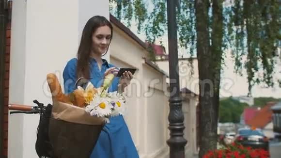 布鲁内特女孩摸着她的头发自拍站在自行车上花和面包在篮子里4k视频的预览图