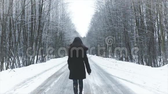 女孩走在通往冬天树林的路上视频的预览图