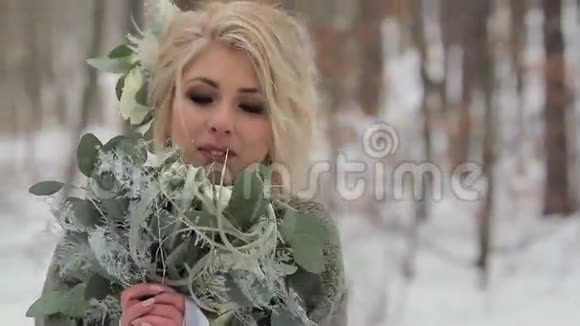 美丽的金发女孩在冬天的森林里捧着花视频的预览图