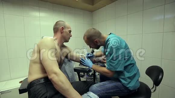 纹身艺术家在工作男人画在他手臂上的女人的脸上快关门纹身沙龙视频的预览图