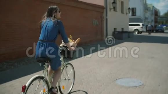 戴着太阳镜的女孩挥舞着黑发在建筑物附近骑自行车汽车停在路边慢悠悠斯泰迪卡姆射击视频的预览图