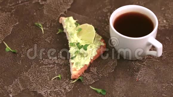 在深色混凝土背景下用牛油果新鲜微绿色和一杯咖啡烤面包视频的预览图