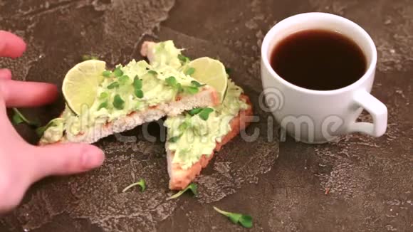 在深色混凝土背景下用牛油果新鲜微绿色和一杯咖啡烤面包视频的预览图