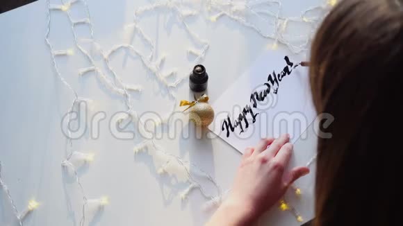 刻字的女主人用墨水在纸上画新年卡片坐在艺术工作室里的花环上视频的预览图
