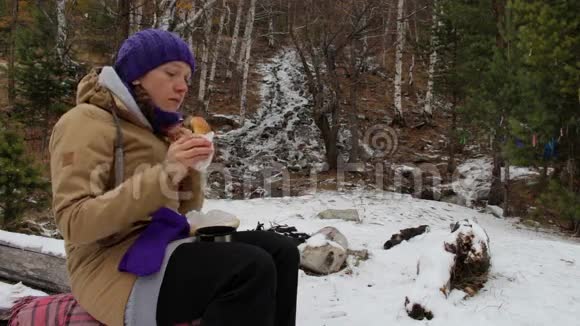 女孩在冬天的树林里小溪边吃蛋糕喝茶视频的预览图