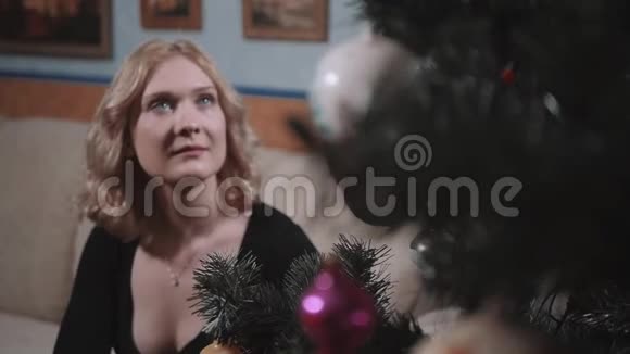 家里圣诞树附近金发的漂亮年轻女人视频的预览图