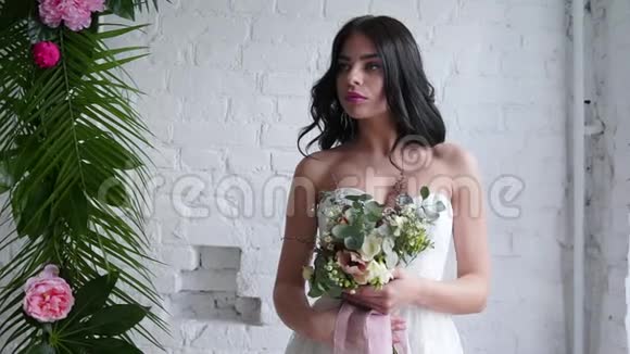 新娘美丽的黑发女子站在婚纱花束靠近窗户视频的预览图