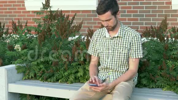 穿着休闲服的男人坐在长凳上用他的智能手机视频的预览图
