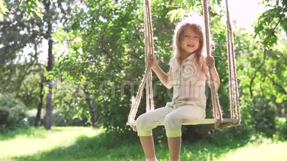 小女孩在夏天公园的秋千上摇摆在树上的绳子上摆动快乐无忧无虑的童年慢慢慢慢视频的预览图