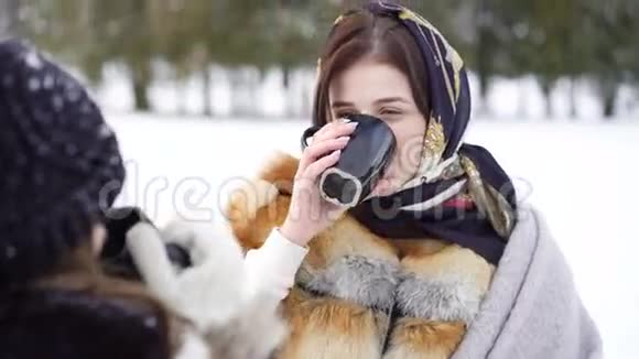 在冬季公园里两个穿着格子布的女孩在说话微笑着喝茶视频的预览图