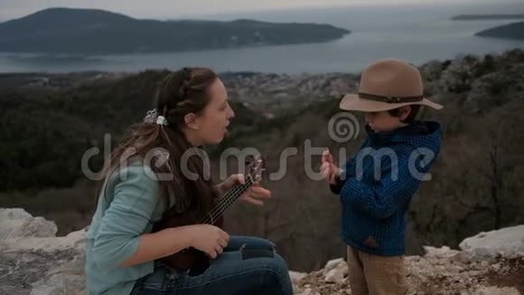 女人在阴天弹吉他小男孩在悬崖上视频的预览图