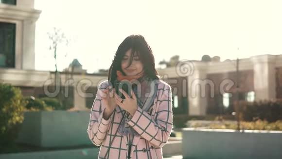 迷人的年轻女人在城市里使用智能手机穿着外套和帽子年轻女子正在给她发短信视频的预览图
