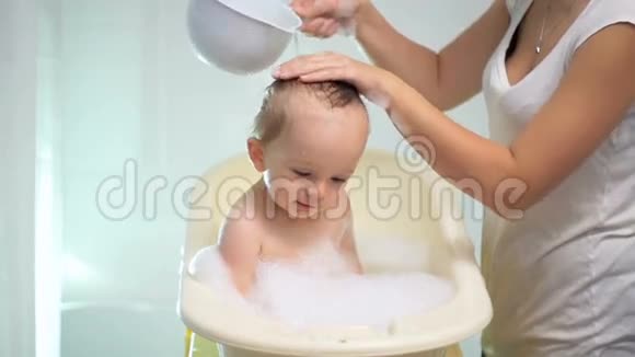 年轻有爱心的母亲在浴室里给孩子洗澡的慢镜头视频的预览图