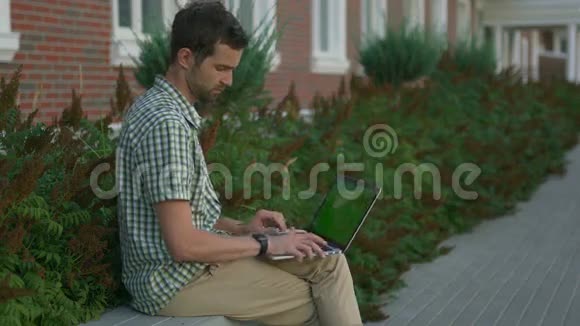 休闲着装的自由职业者坐在长凳上用他的智能手表和笔记本电脑视频的预览图