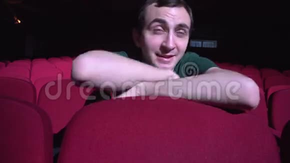 一个男人坐在黑色电影院里舒适的红椅子上看着喜剧和笑声视频的预览图
