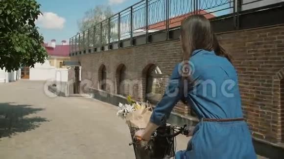一个穿着衣服的女孩骑着自行车花篮里的花触碰树叶慢的稳定的镜头视频的预览图