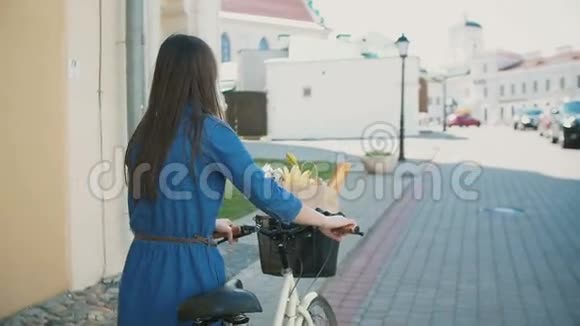 一个挥舞着头发的女孩走在自行车上带着花和面包在篮子里慢悠悠稳定的镜头视频的预览图