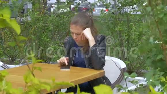 悲伤的漂亮女孩坐在咖啡馆的桌子旁在智能手机上读取短信悲伤和渴望绝望视频的预览图