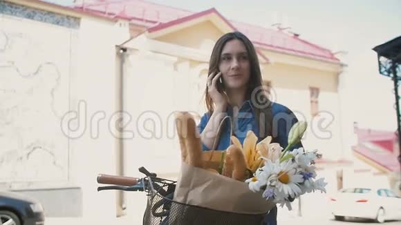 年轻的黑发女人站在街上用一辆带篮子的自行车打电话最后挂断了电话慢悠悠视频的预览图