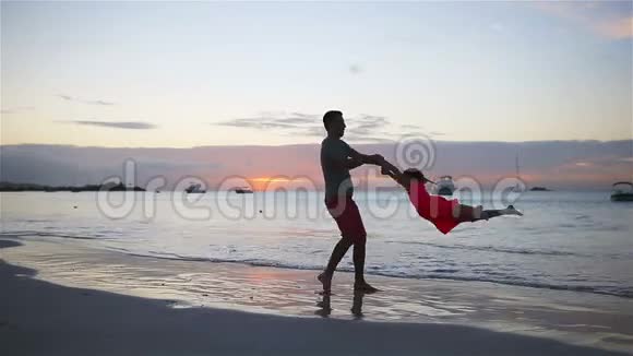 小女孩和快乐的爸爸在海滩度假时享受日落的乐趣视频的预览图