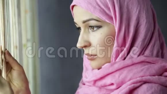 美丽的穆斯林阿拉伯妇女身穿粉红色头巾望着窗外视频的预览图