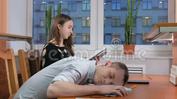 疲惫的学生睡觉的人带着耳机在笔记本上的讲座在这女人身边为所有人努力记录视频的预览图