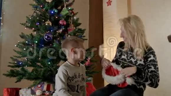 母亲和儿子在圣诞树下戴着圣诞老人的帽子视频的预览图