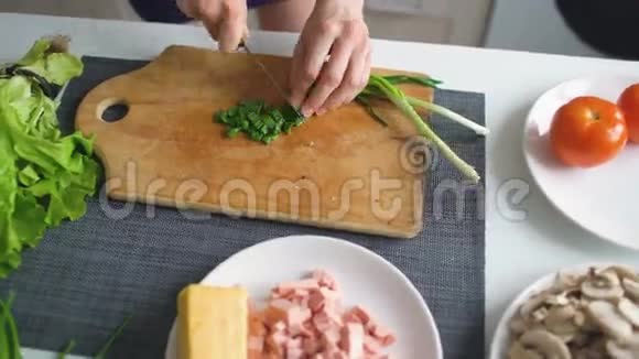 在家里的厨房里用女孩的手在木板上切葱做披萨视频的预览图