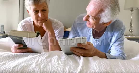 老人使用数码平板电脑而妇女则在床上看书视频的预览图